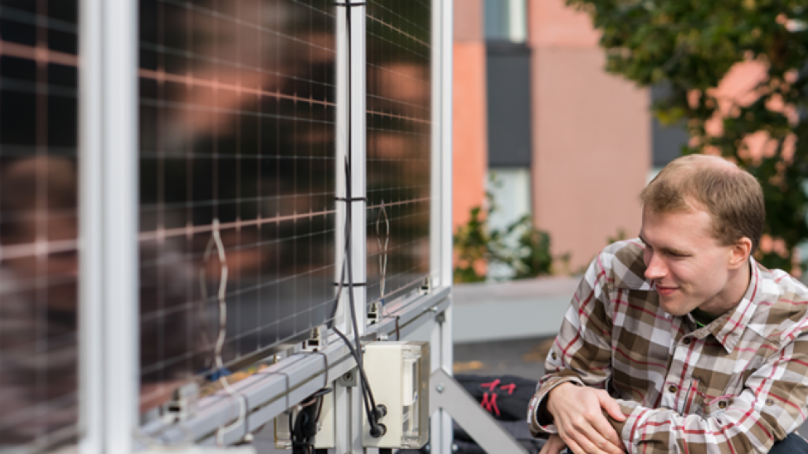 Tutkija Sami Jouttijärvi katselee pystyyn asennettuja kaksipuolisia aurinkopaneeleita kyykistyneenä niiden viereen Turun AMK:n katolla kesällä