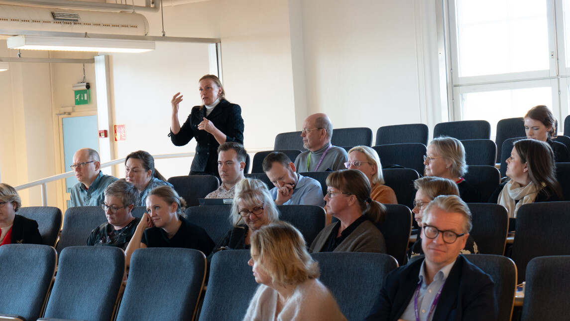 Pirjo Mustonen puhumassa penkkirivillä ja yleisö kuuntelemassa