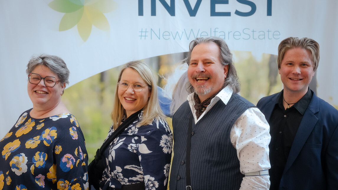 neljä ihmistä seisoo hymyilevinä INVEST-messuseinän edessä