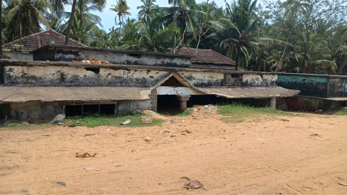Sandy beach with derelict buildings behind showing some water damage.