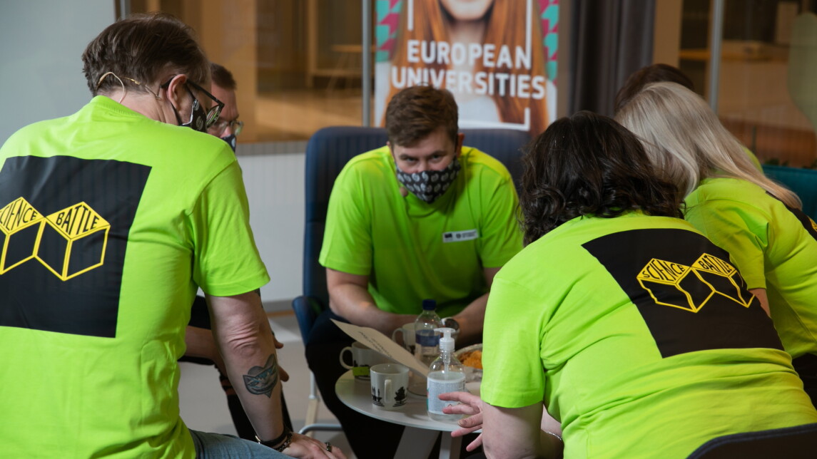 Kuusi henkilöä istuu pienen pöydän ääressä yllään neonvihreät kisapaidat.