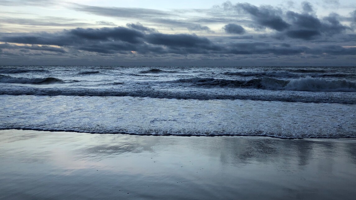 Blueish picture of a sandy seashore with waves rolling on the beach.