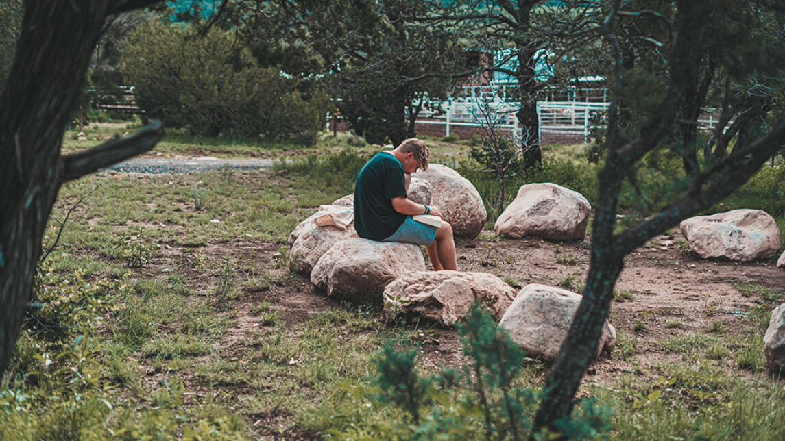 Poika istuu kivellä metsässä.