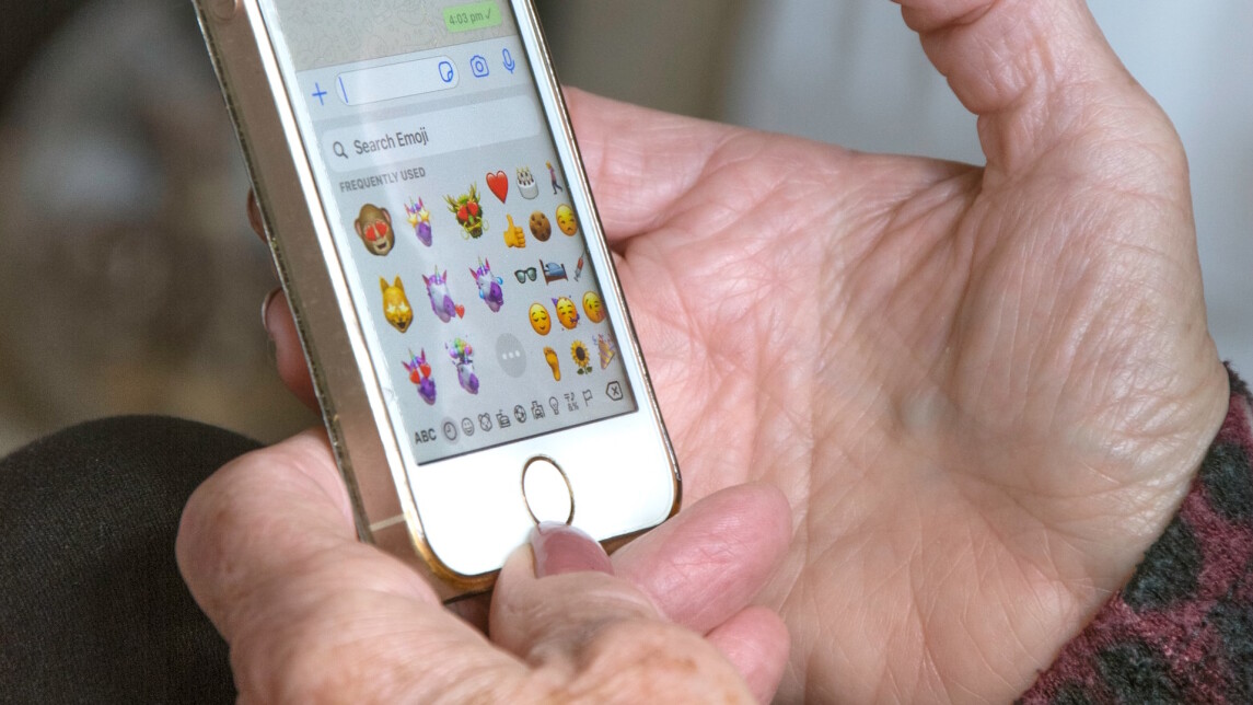 Emojeja kännykän ruudulla, kännykkää pitelevät vanhemman naisen kädet