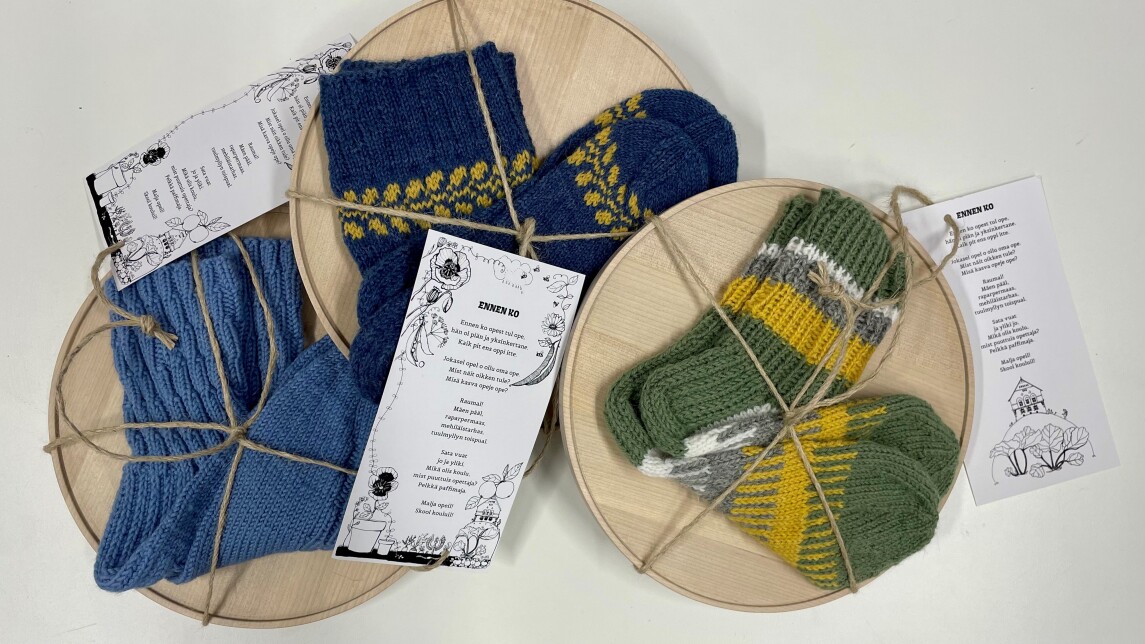 Pakettinarun sisälle kiedottu puinen lautanen ja villasukat. Narussa Heli Laaksosen kirjoittama murreruno.