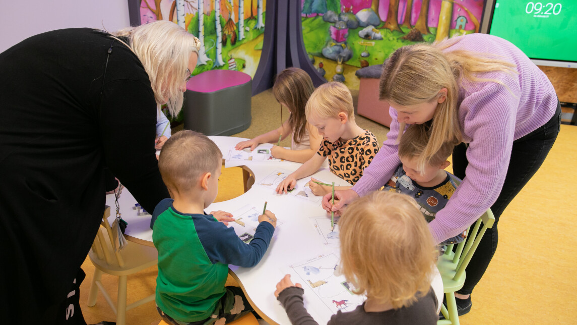 Pieniä lapsia pöydän ääressä varhaiskasvatuksen ammattilaisen kanssa.