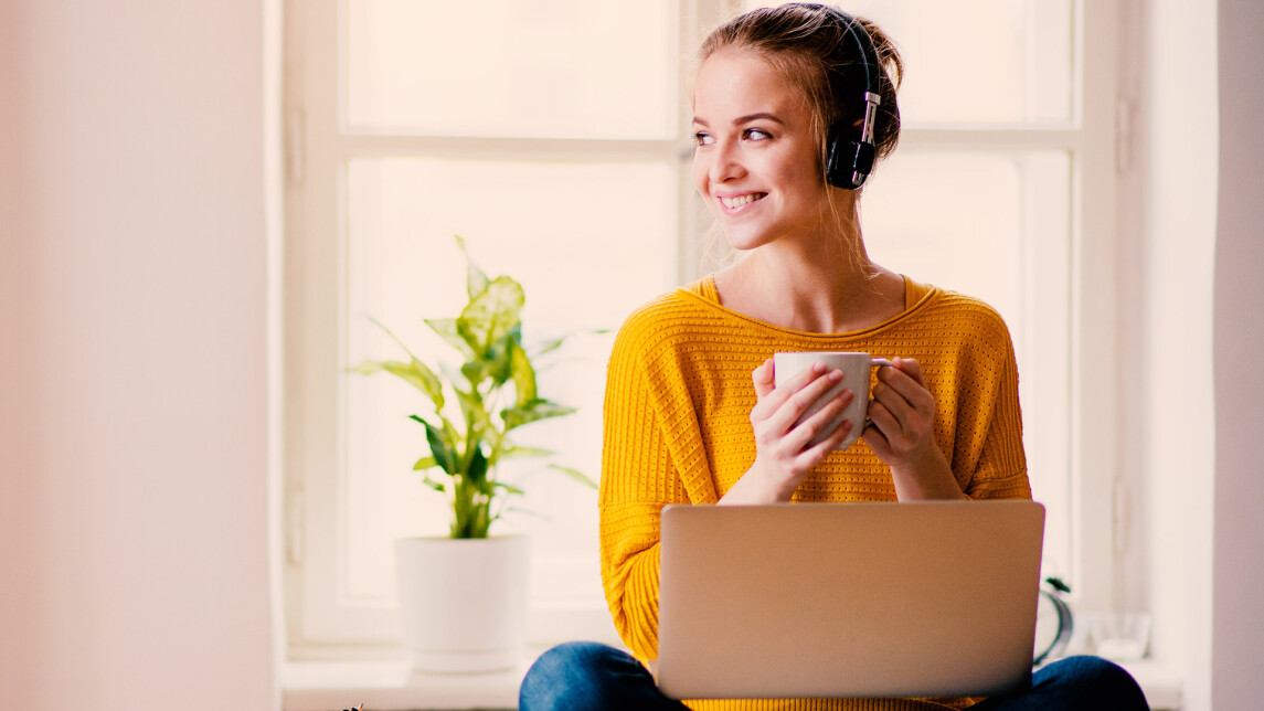 Opiskelija kuulokkeet päässä ja kannettava tietokone sylissä juo kahvia.