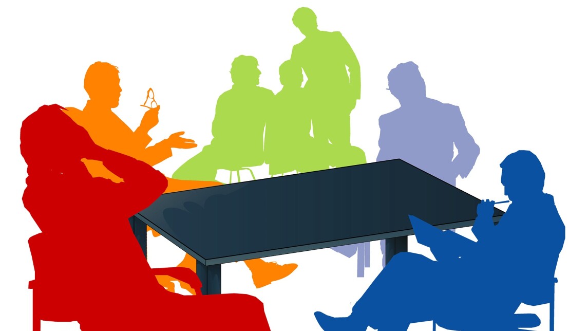 Ihmisiä istumassa palaveripöydän ääressä.