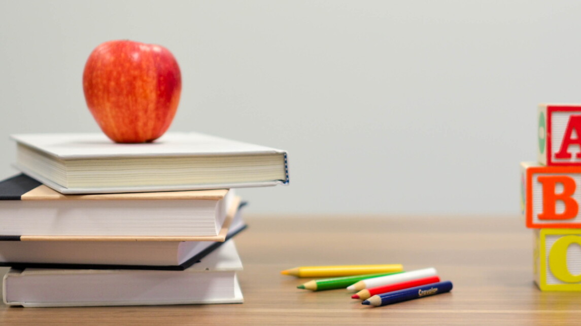 Omena, oppikirjoja, värikyniä ja kirjainpalikoita pöydällä