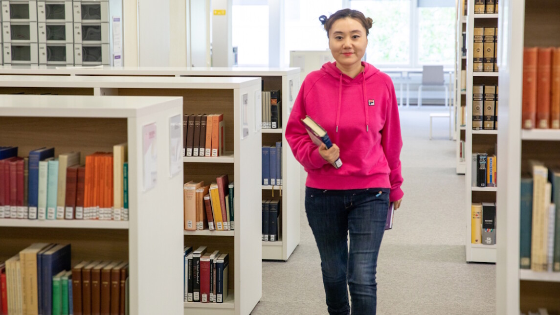 Opiskelija kävelee kirjastossa kirjoja kädessään.