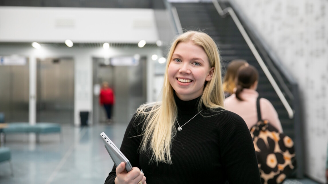 Opiskelija on menossa luennolle yliopiston aulassa läppäri mukanaan.