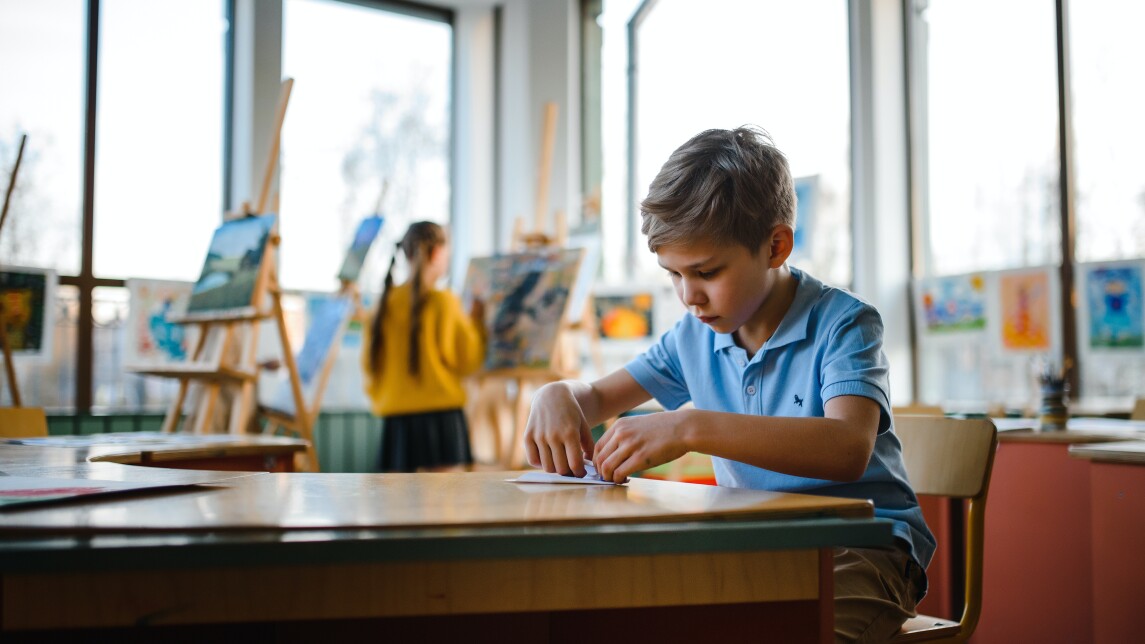 Poika istuu luokkahuoneessa pöydän äärellä.