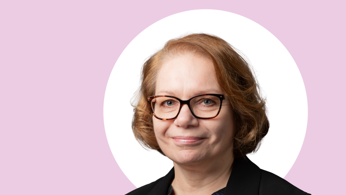 Marjo Kaartinen lähikuvassa, taustalla vaaleanpunaista ja valkoista.