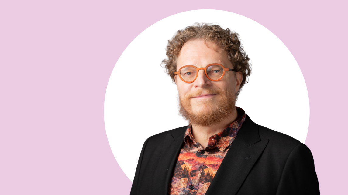 Tapio Salakoski lähikuvassa, taustalla vaaleanpunaista ja valkoista.