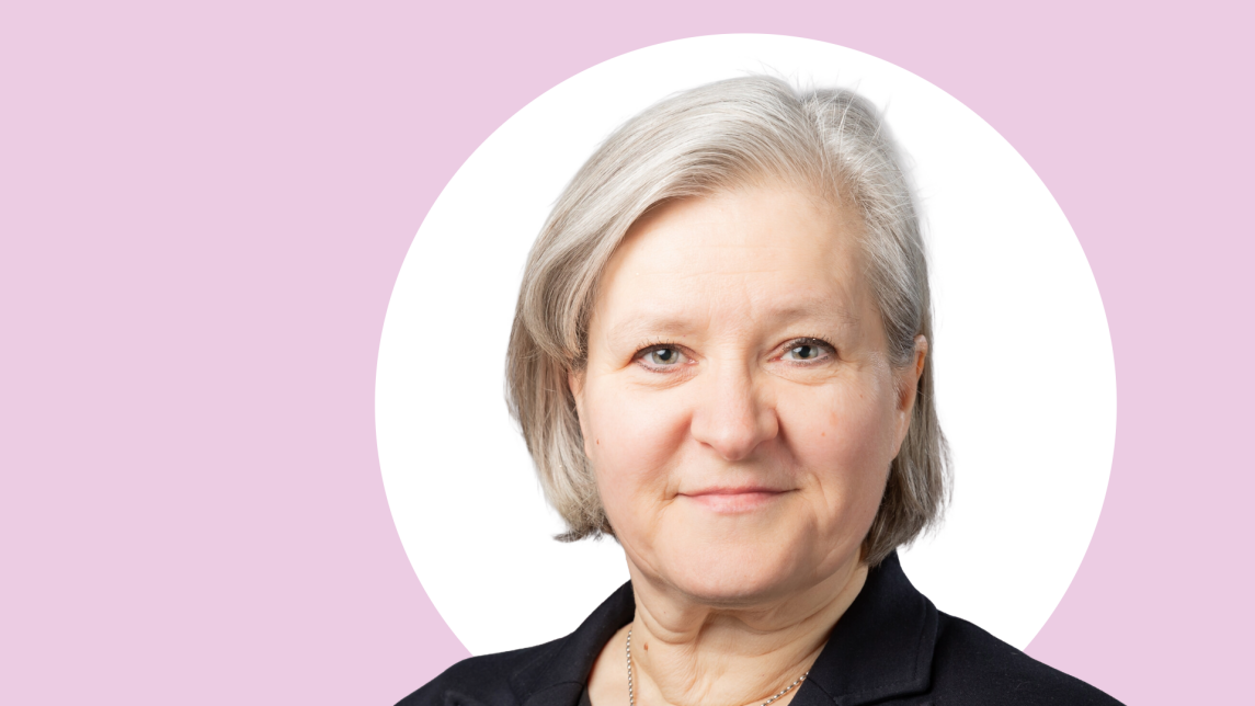 Kirsi Virtanen lähikuvassa, taustalla vaaleanpunaista ja valkoista.
