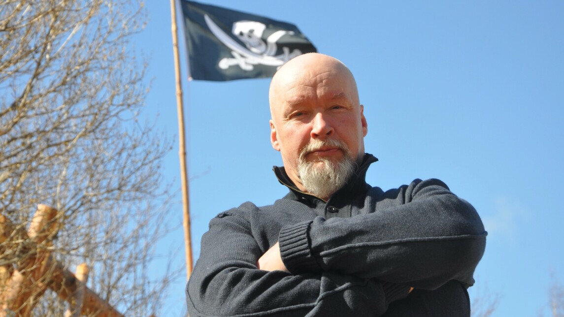 Tuomas Kuhmonen ulkona lähikuvassa, taustalla salossa merirosvolippu.