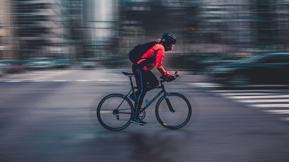 Punaiseen ja mustaan pukeutunut ihminen polkee tiellä vauhdikkaasti.