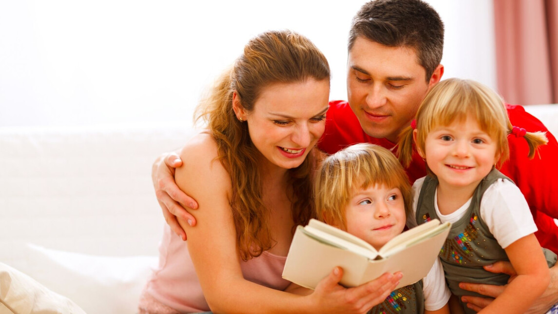 Isä, äiti ja kaksi lasta istuvat sohvalla, äiti lukee lapsille kirjaa