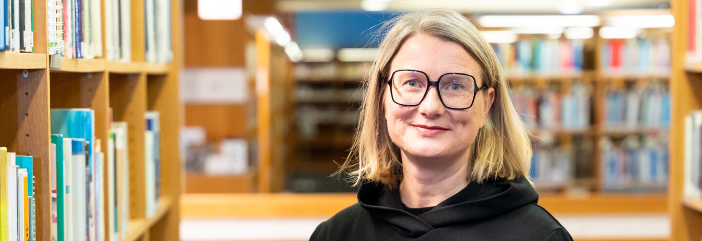 Johanna Kaakinen kirjastossa kirjahyllyjen välissä.