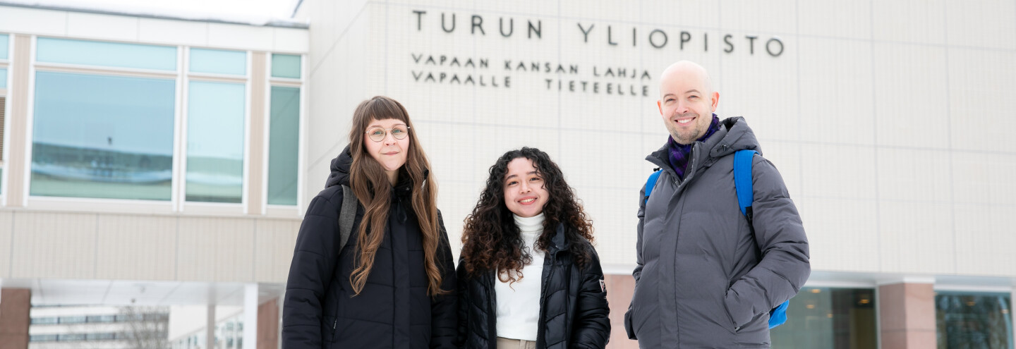 Three people in front of the university's main building with snow present