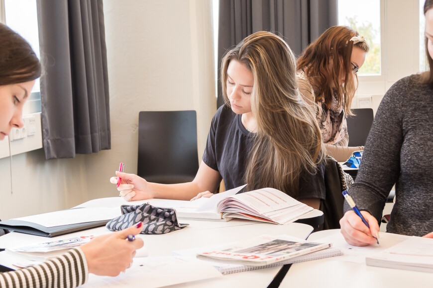 Kolme opiskelijaa luokassa tekee tehtäviä oppikirjasta