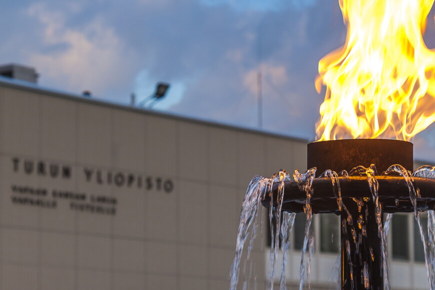 Etualalla suihkulähteen soihtu palamassa, taka-alalla Turun yliopiston päärakennus.
