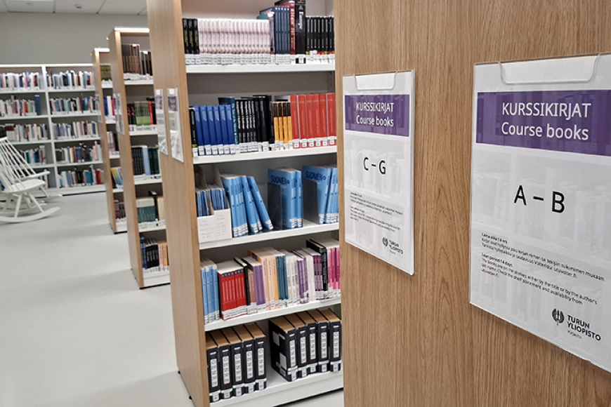 Kurssikirjahyllyjä Arcanumin kirjastossa, taustalla valkoinen keinutuoli.