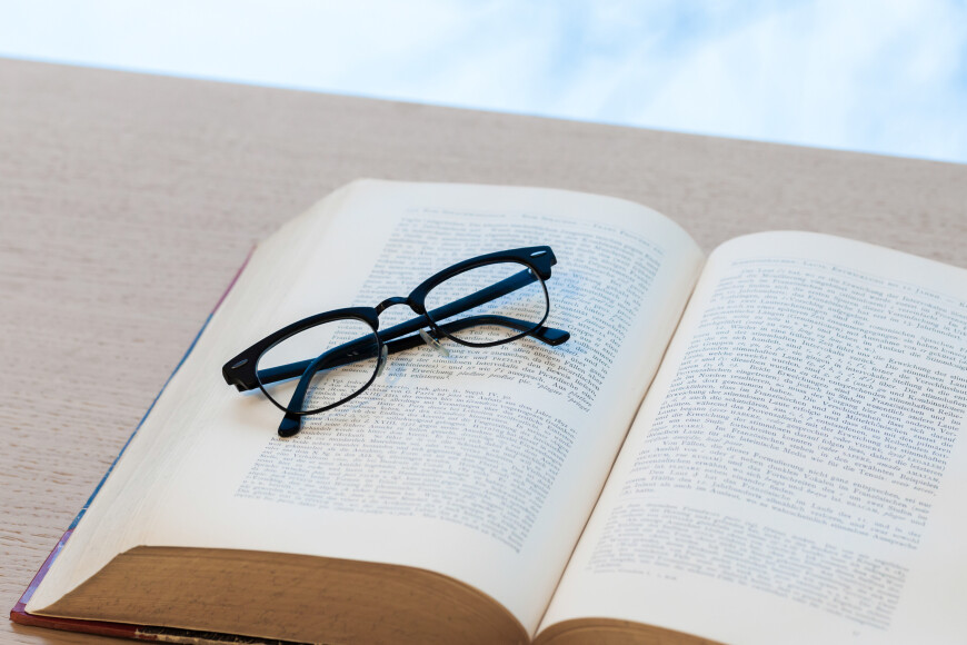 Mustat silmälasit kirjan päällä ikkunan luona