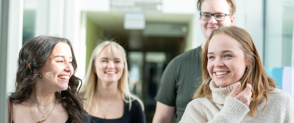 Neljä hymyilevää opiskelijaa Publicumin käytävällä
