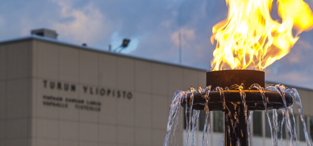 Etualalla suihkulähteen soihtu palamassa, taka-alalla Turun yliopiston päärakennus.