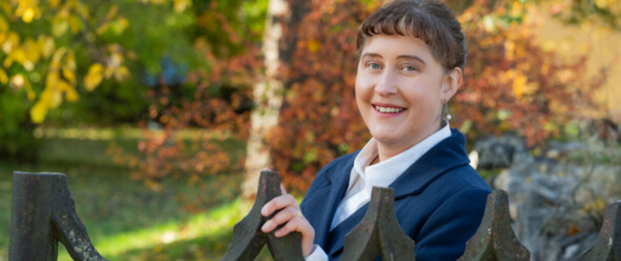 Ulla Ahlmen-Laiho lähikuvassa ulkona vanhan rautaisen portin edessä, taustalla näkyy puita joissa on värikkäät lehdet.