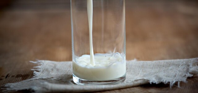 Pöydällä lasi, johon kaadetaan maitoa.