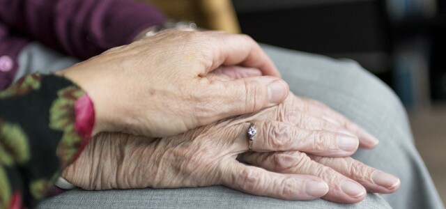 hoitavan henkilön käsi pitää ikääntyneen henkilön kädestä