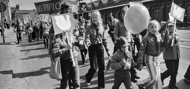 Vappumarssijoita Hämeentiellä. Edessä lapset kantavat kylttejä, joissa rauhankyyhkyn kuva. Keskellä edessä lapsi ilmapallon kanssa. Takana kannetaan banderollia, jossa teksti: Meripioneerit.