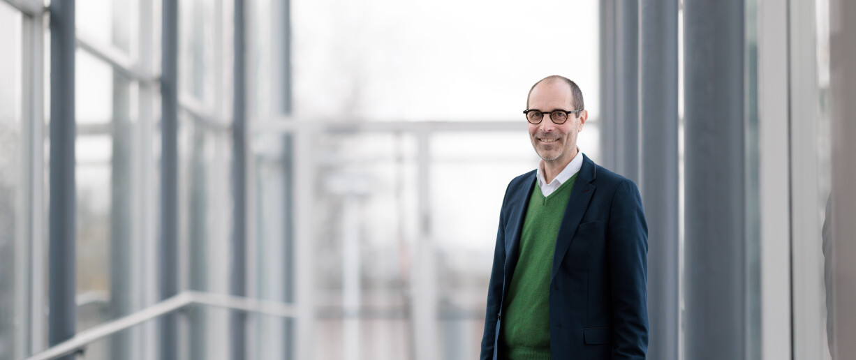 Dekaani Jaakko Järvi henkilökuvassa valoisalla lasiseinäisellä käytävällä kampuksella