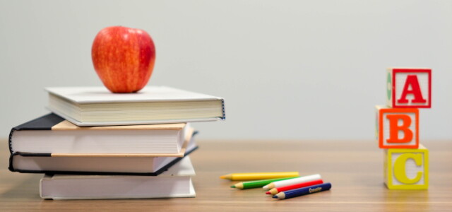 Omena, oppikirjoja, värikyniä ja kirjainpalikoita pöydällä