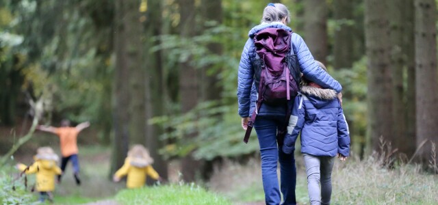 An adult walking along a forest path with their arm around a child walking beside them.