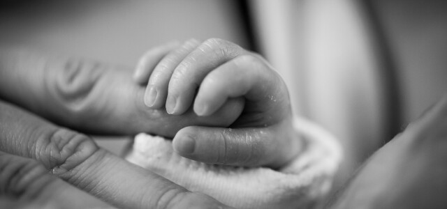 Mustavalkoinen kuva vauvan kädestä pitämässä kiinni aikuisen sormesta