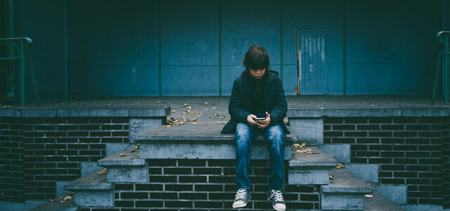 Poika istuu rappusilla puhelin kädessä