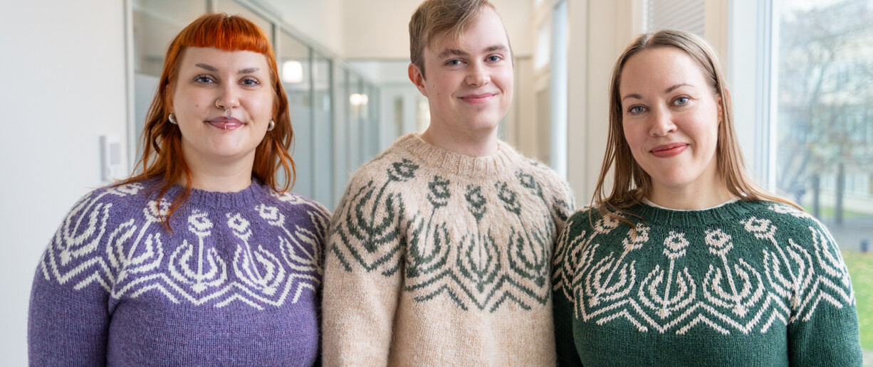 Kolme henkilöä Turun yliopiston soihtu-neuleet päällä.