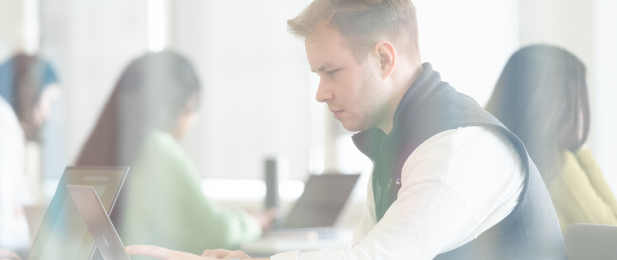 A person working on a laptop, with other people in the background.