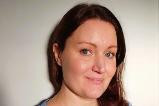 Nainen hymyilee kameralle seinän edessä.