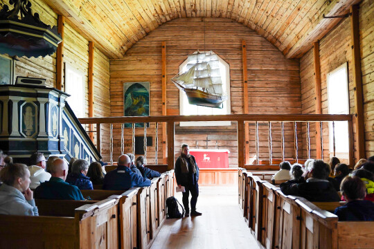 Tutkija Sofia Paasikivi seisoo Seilin vanhan puukirkon penkkirivien välissä yleisön edessä ja yleisö kuuntelee kun tutkija kertoo kirkon kryptoista