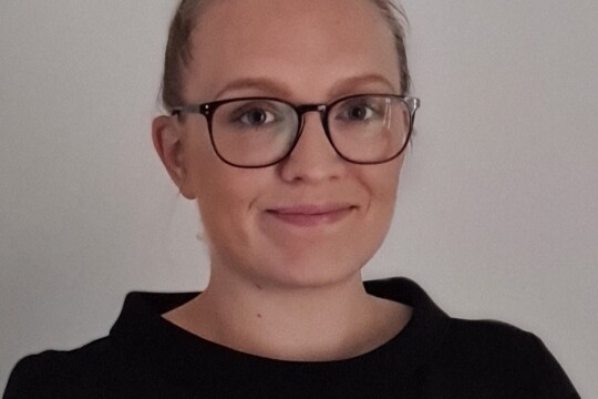 Vaaleahiuksinen, mustaan paitaan pukeutunut nainen katsoo hymyillen kameraan.