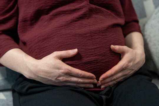 Äiti pitää käsiä raskausvatsansa päällä.