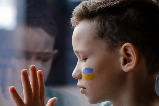 Lapsi ikkunalla, kasvoihin maalattu Ukrainan lippu.