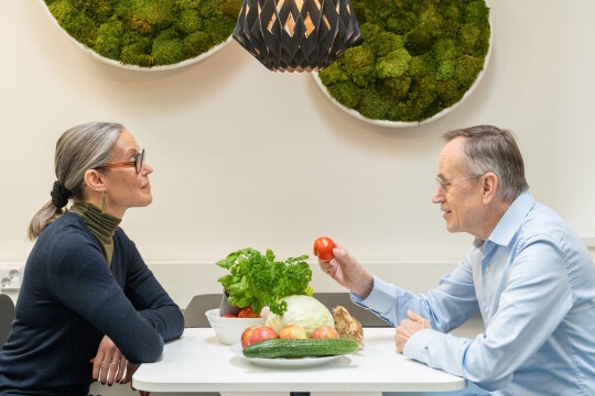 Kati Hanhineva ja Jorma Toppari istuvat vastakkain pöydän ääressä. Pöydällä on tuoreita kasviksia.