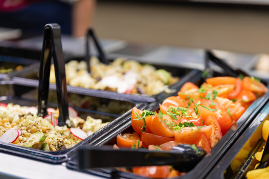 lähikuvassa itsepalveluravintolan linjaston salaattikippoja, joissa tomaattilohkoja ja salaatteja sekä ottimia