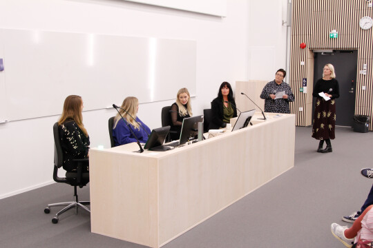 Panelistit puhumassa luentosalin edessä