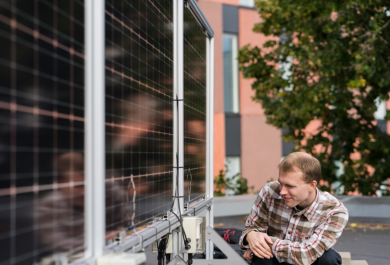 Tutkija Sami Jouttijärvi katselee pystyyn asennettuja kaksipuolisia aurinkopaneeleita kyykistyneenä niiden viereen Turun AMK:n katolla kesällä
